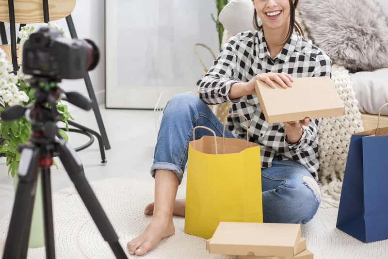 A woman is unboxing products in front of a camera while sitting on the floor.