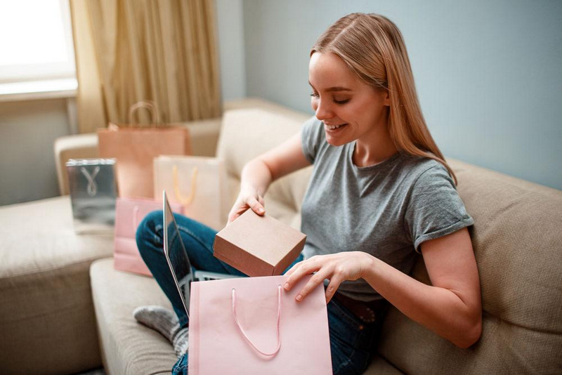 A woman sitting on a couch and smiling while opening a gift box.