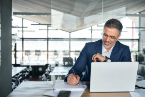 A businessman in a modern Dubai office reviews documents and checks his watch, emphasizing time management.