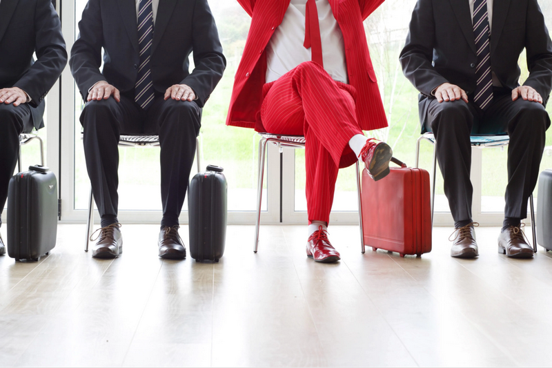 Three seated men in business attire with the middle person wearing a bright red suit.