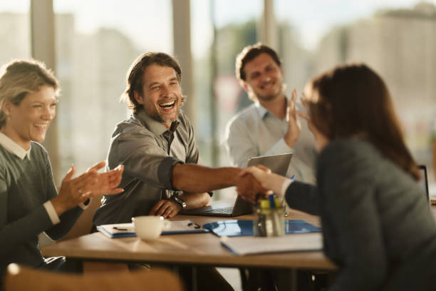 Business professionals joyfully shaking hands and applauding in a modern office setting.